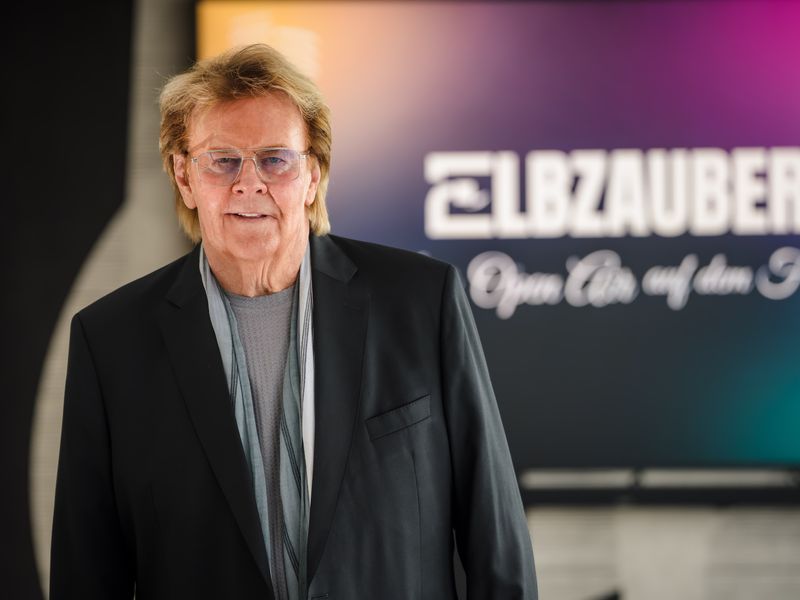 Howard Carpendale ist einer der Künstler beim "Elbzauber". Hier steht er vor einem Bildschirm mit der Headline der Veranstaltung.